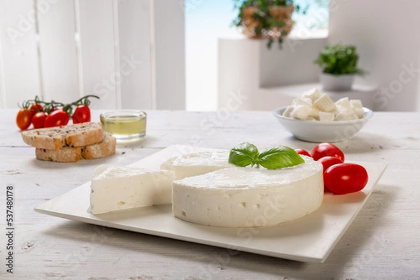 Fototapeta fresh cheese with slice and basil leaf, tomatoes, olive oil, on white square plate, placed on a white wooden table