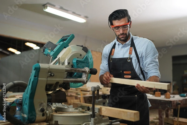 Fototapeta Contemporary Carpenter Working, Portrait of modern carpenter making wood furniture while working in joinery lit by sunlight with factory background on small business concept, copy space