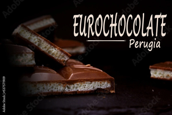 Fototapeta Pieces of milk aerated chocolate close-up on a dark background with an inscription. The concept of the Perugia Chocolate Festival