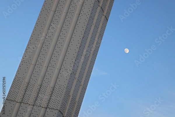 Fototapeta Abstract minimalist picture of riveted steel frame structure, part of the Elizabeth Bridge (Erzsébet híd) in Budapest, Hungary in front of blue sky and moon. 
Color architectural close-up detail photo