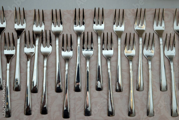 Fototapeta A large pile of shiny stainless steel forks neatly arranged on the laid table. Abstract illustration photo of cutlery, restaurant or catering.