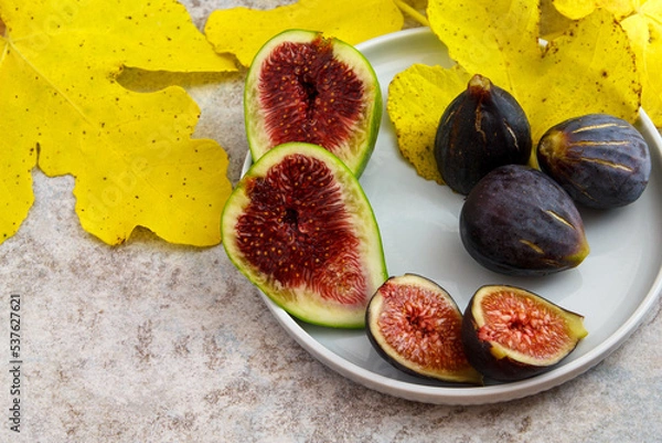 Fototapeta Feigen reif geschlossen aufgeschnitten mit gelbem Feigenblatt auf Teller 