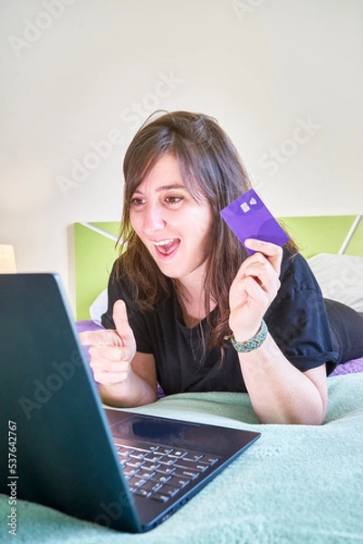 Fototapeta Vertical shot of a young white Caucasian girl doing a transaction with a bank card and a laptop