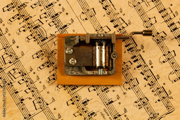 Fototapeta Music box and notes. Souvenir Music box on the background of old notes. Hand organ for classical and modern melody. Retro cylindrical mechanism with hand-cranked movements on wooden stand. Top view
