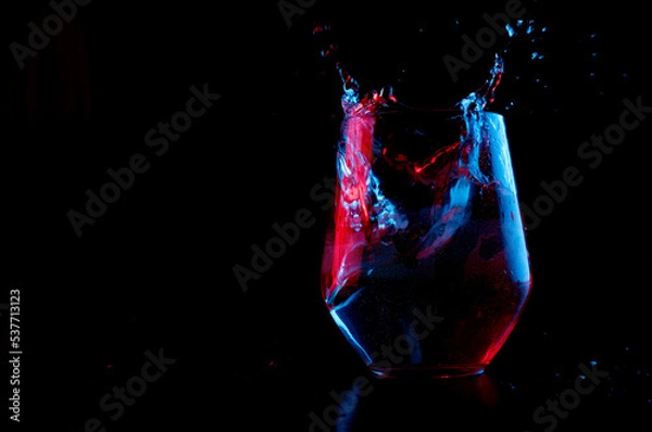 Obraz Water highlighted in blue and red splashing into a glass