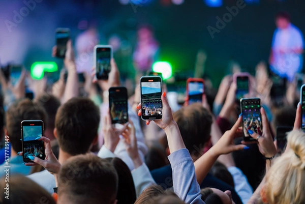 Fototapeta Hands raised up with smartphones recording videos of the music performance on a stage 