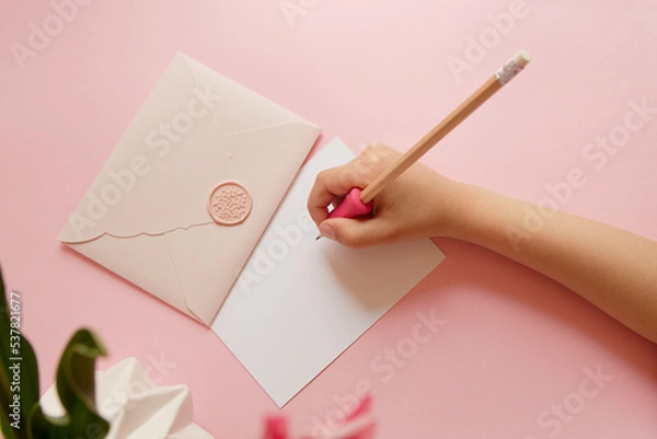 Fototapeta Top view of hands of anonymous child holding pink envelope with gift certificate.Good for mother day.