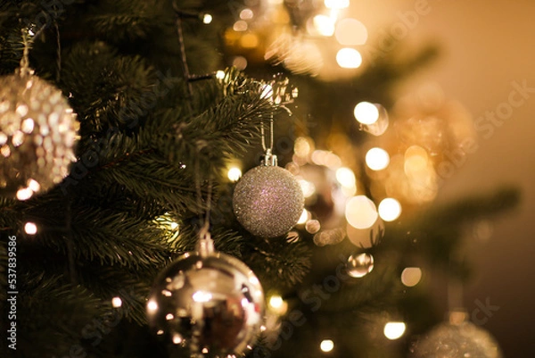 Fototapeta Close up view of beautiful fir branches with shiny golden bauble or ball, xmas ornaments and lights, Christmas holidays background. copy space. Decoration on christmas tree. Festive new 2023 year
