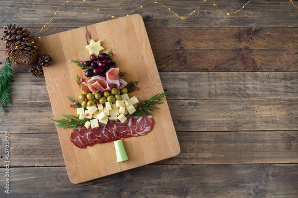 Fototapeta Christmas tree shaped cheese and charcuterie board with wooden background. Top view. Copy space.