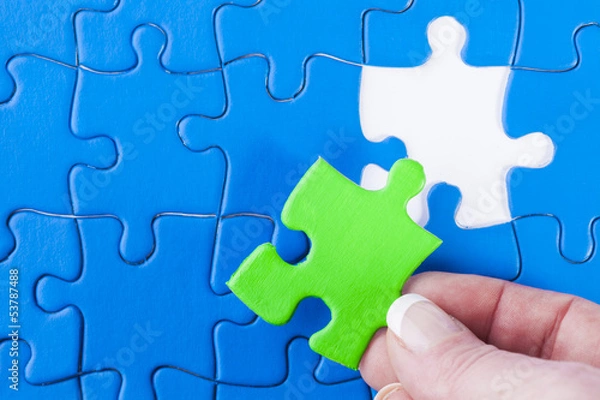 Fototapeta Woman's hand placing missing piece in Jigsaw puzzle  signifying