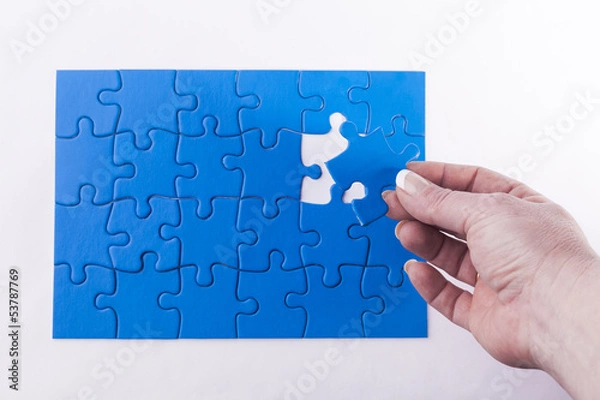 Fototapeta Woman's hand placing missing piece in Jigsaw puzzle  signifying