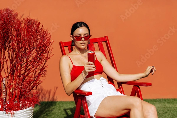 Obraz A girl on an orange background with a red tin can in her hands. Cheerful girl, advertising shooting