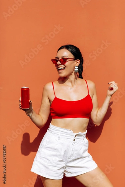 Obraz A girl on an orange background with a red tin can in her hands. Cheerful girl, advertising shooting