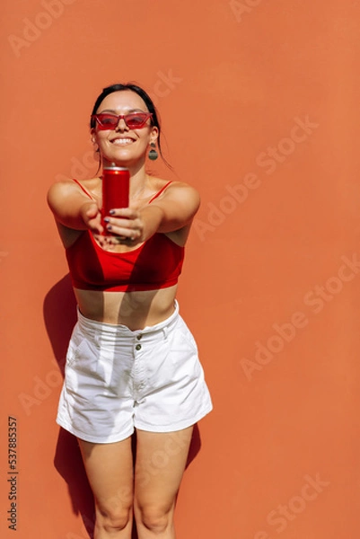 Obraz A girl on an orange background with a red tin can in her hands. Cheerful girl, advertising shooting