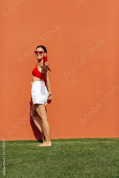 Obraz A girl on an orange background with a red tin can in her hands. Cheerful girl, advertising shooting