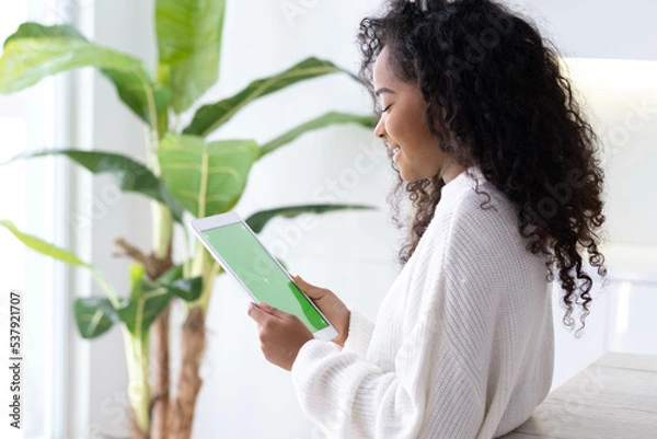 Fototapeta African American black girl using iPad tablet viewing green screen press browsing chroma key online typing text reading social media . Freelancer Remotely working online at home 