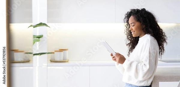 Fototapeta Banner African American Girl using iPad tablet at home pressing finger, reading social media internet, typing text or shopping online. Freelancer Remotely working online at home
