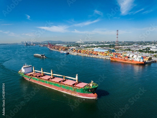 Fototapeta Aerial view of a fully loaded cargo ship leaving the Montreal Port and going downriver on the St.Lawrence River.