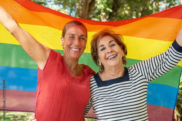 Fototapeta A middle-aged girl next to an older lady raising the gay rainbow flag. Support for the lgbti+, gay, homosexual, bisexual, lesbian, trans, non-binary community. Fight for the freedom and rights