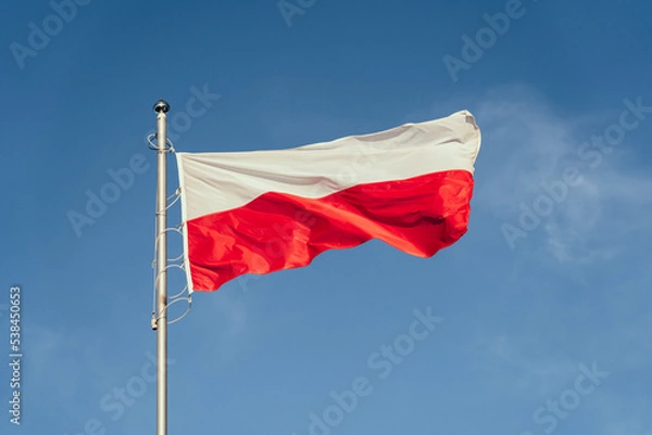 Obraz Polska flaga biało-czerwona powiewająca na maszcie na tle błękitnego nieba