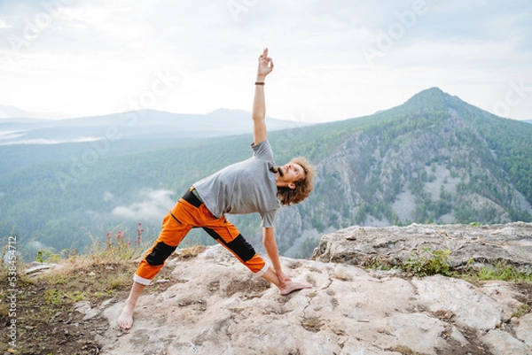 Obraz Utthita Trikonasana pose of an elongated triangle, a guy practices yoga standing on top of a mountain, body warm-up, asana triangle, zen meditation in nature