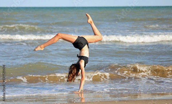 Obraz barefoot girl in black swimsuit from rhythmic gymnastics exercises on the seashore