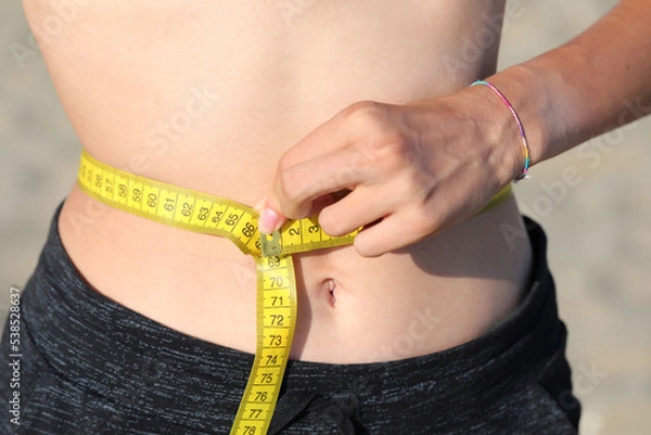 Fototapeta skinny girl measures your waist with a flexible tape measure and measures in centimeters