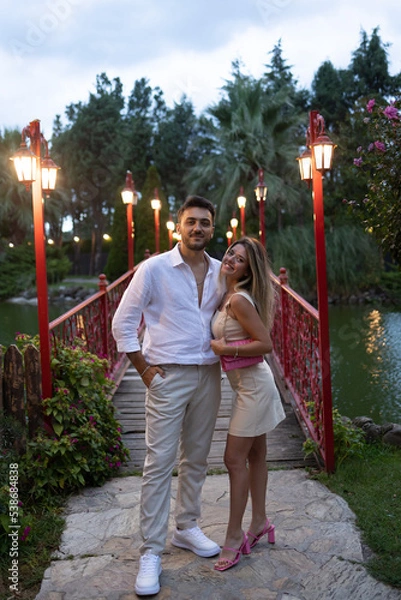 Fototapeta Young couple on romantic date. Kissing on the bridge. Hug each others.
