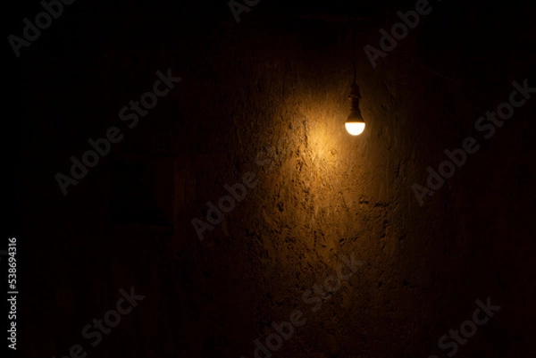 Fototapeta Bombilla encendida en cuarto oscuro