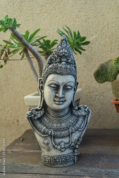 Fototapeta buddha head on wooden table surrounded by plants