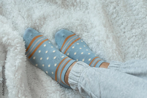 Obraz Women's legs in socks and warm gray pants on a white fluffy plaid, at home in a cozy autumn season. Rest at home after a hard day's work.
