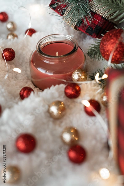 Obraz Decor of red shiny Christmas balls, gifts in a checkered package decorated with a burlap ribbon, lights of a Christmas garland on a white fluffy soft background. Cozy holidays. New Year holidays 2023.
