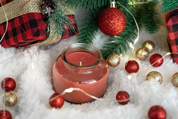 Obraz Red candle,gifts in a checkered cloth wrapper, yellow lights on a garland, a sprig of a Christmas tree on a white soft background.  Postcard for the New Year and Christmas.