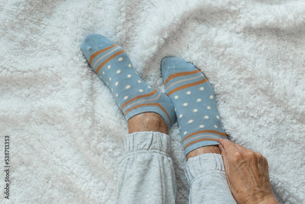 Obraz Women's hands put on socks higher while sitting on a white fluffy plaid. Cozy cold autumn time to stay at home. Top view 