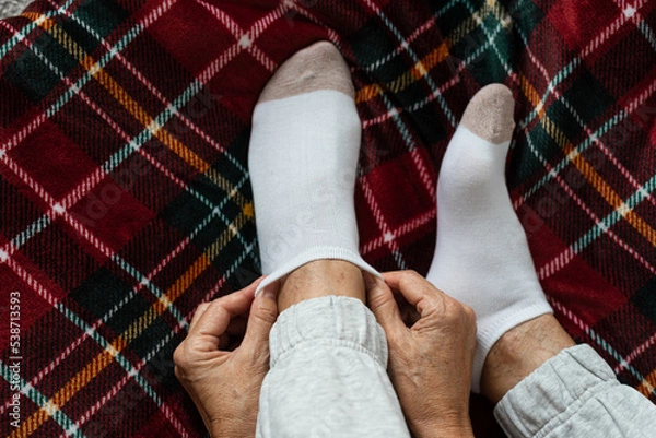 Obraz Women's hands put socks on legs sitting on a red checkered plaid. Rest at home after a hard day's work.