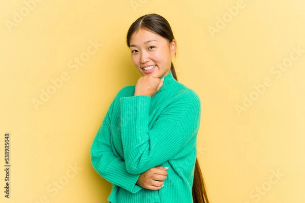 Fototapeta Young Asian woman isolated on yellow background smiling happy and confident, touching chin with hand.