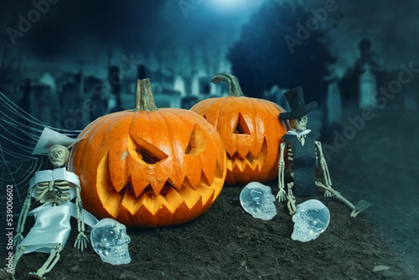 Fototapeta Halloween's decoration with two pumpkins, zombie husbands and skulls, in the cemetery. Halloween's night.