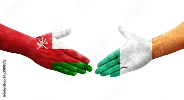 Fototapeta Handshake between Ireland and Oman flags painted on hands, isolated transparent image.