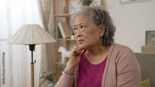 Obraz depressed asian old lady feeling loneliness and burying face in hands while worrying about problems in the living room at home.