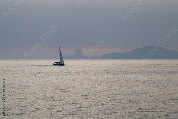 Fototapeta Sailboat sailing in the Mediterranean during sunset with an island behind