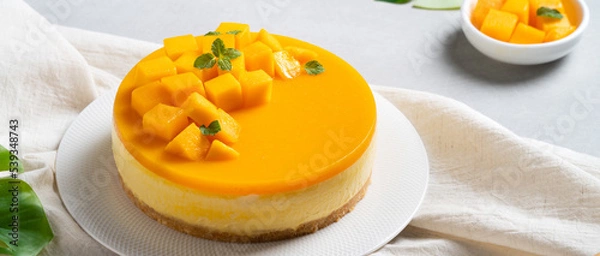 Fototapeta Delicious glazed mango no baked cheese cake with fresh diced mango pulp topping on bright table background.