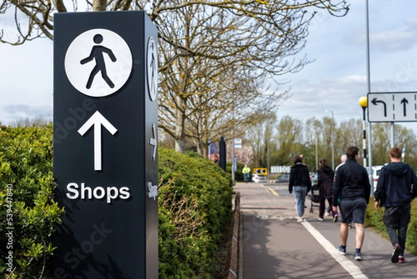 Fototapeta Multidirectional wayfinding sign with arrow and person walking icon pointing towards shops. 