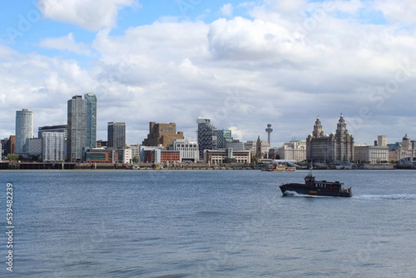 Fototapeta A beautiful image of the famous Liverpool Skyline and cityscape with the River Mersey in front. A speed boat and the ferry can be seen on the River.
