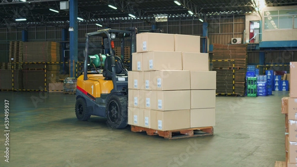 Obraz A forklift is containing stacked cargo cardboard boxes on wooden pallet in a large warehouse for preparing to ship with logistics transportation. A lot of boxes are filled with goods for distribution.