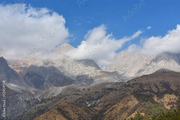 Fototapeta 
panoramic view of the mountain range in the clouds with blue sky on the background in Arslanbob in Kyrgyzstan