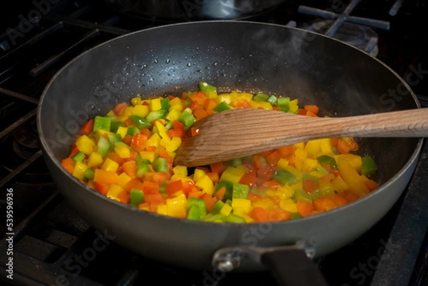 Fototapeta Close up, selective focus on diced bell peppers cooking in a large skillet on a gas stove top