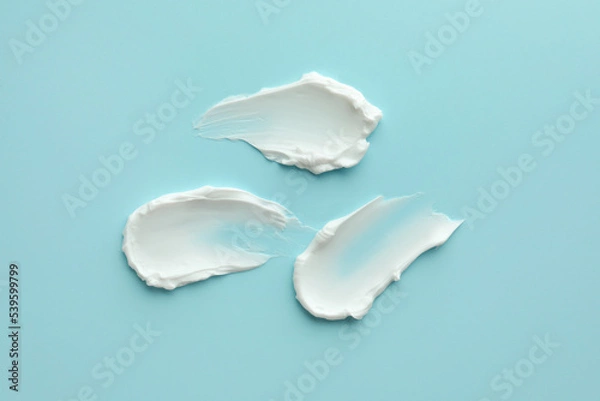 Fototapeta Samples of face cream on light blue background, top view