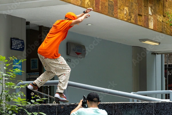 Fototapeta young man dressed in orange skating in a shopping mall doing tricks as a manual