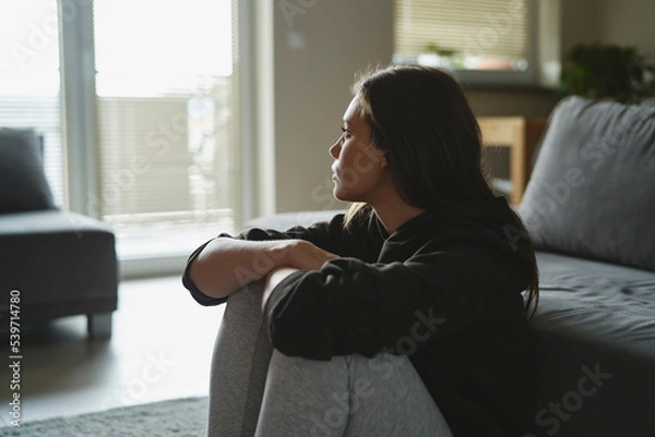 Obraz Caucasian sad woman sitting at the floor and looking throw window at home