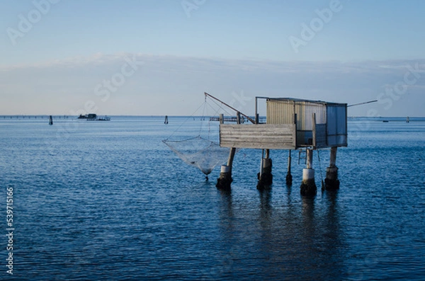 Fototapeta Un casone da pesca con una barca che passa visto dall'isola di Pellestrina in una giornata invernale